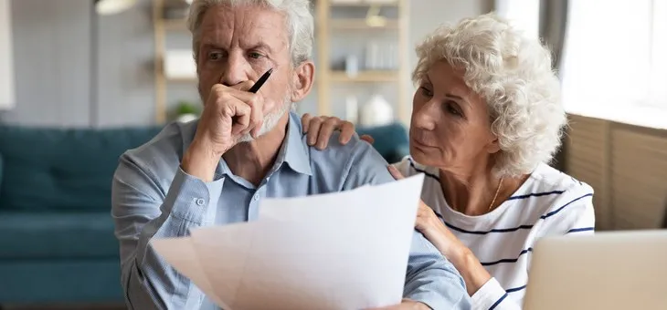 Una pareja de adultos mayores revisa documentos financieros con expresión de preocupación en su hogar