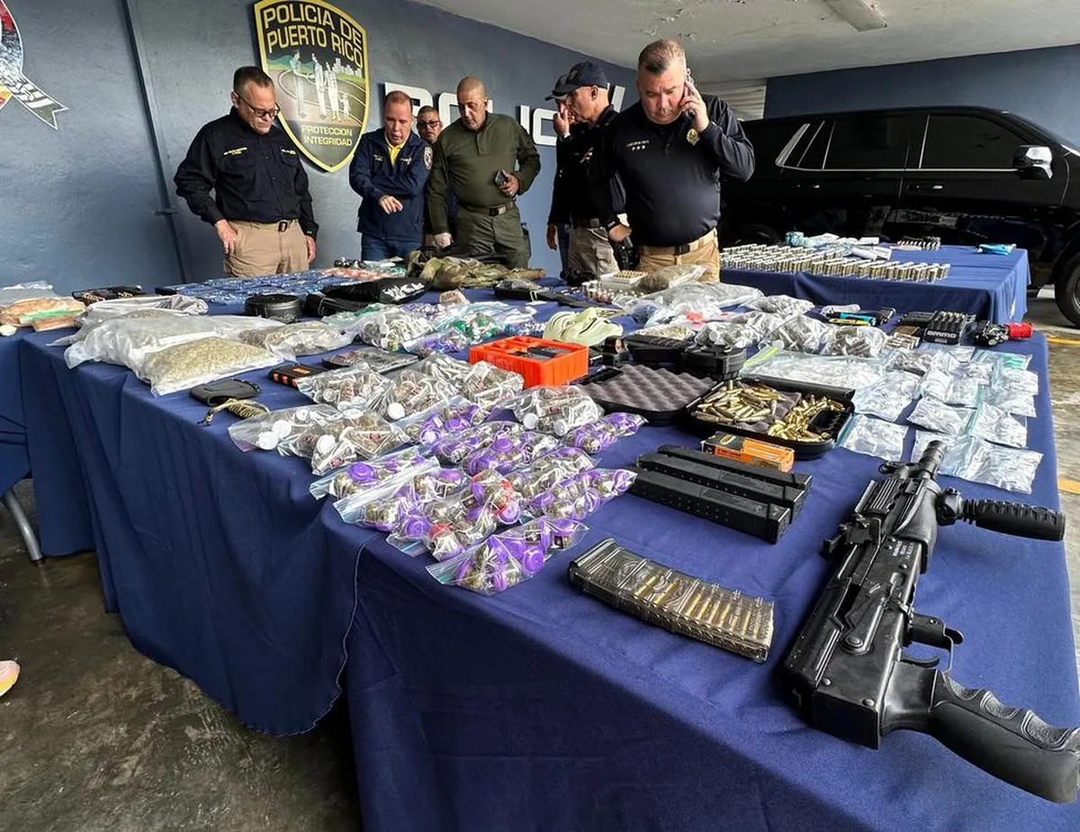 Oficiales de la Policía de Puerto Rico de pie detrás de una mesa cubierta con bolsas de droga, armas largas, cargadores y municiones ocupadas en un operativo policial