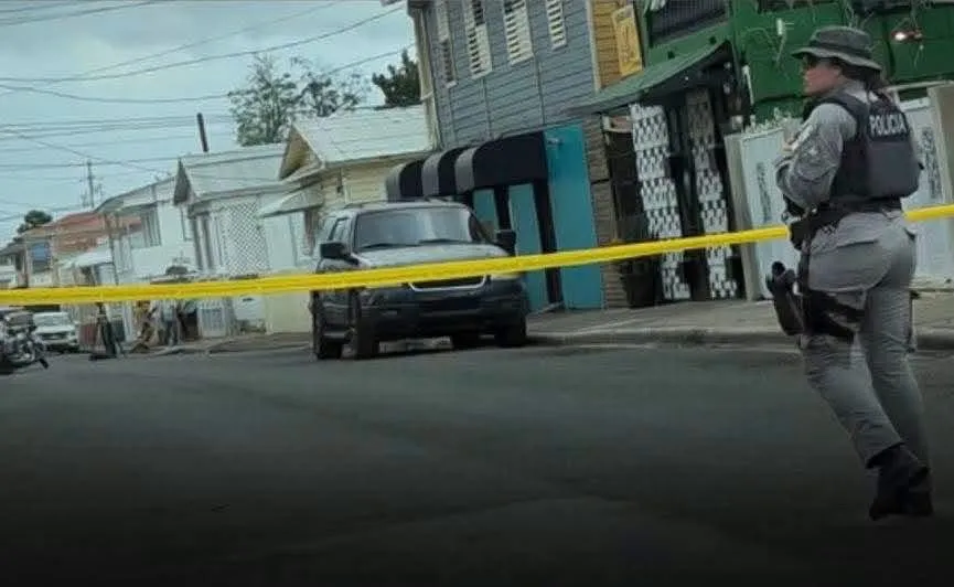 Fotografía de una calle de Ponce acordonada con cinta amarilla de la Policía, con una agente de pie junto a la escena del crimen.