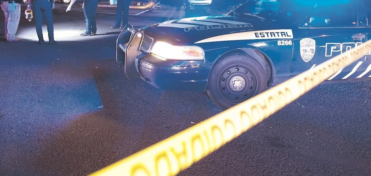 Patrulla de la Policía estatal con las luces encendidas detrás de una cinta amarilla de escena de crimen durante la noche