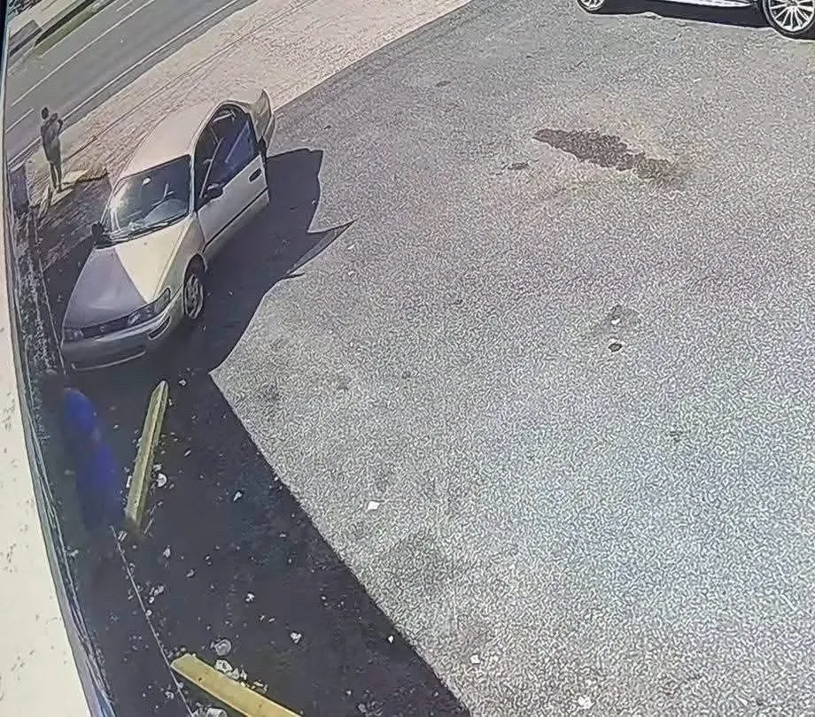 Vista amplia de una cámara de seguridad: un sedán color crema y una figura al fondo, junto a la calle.