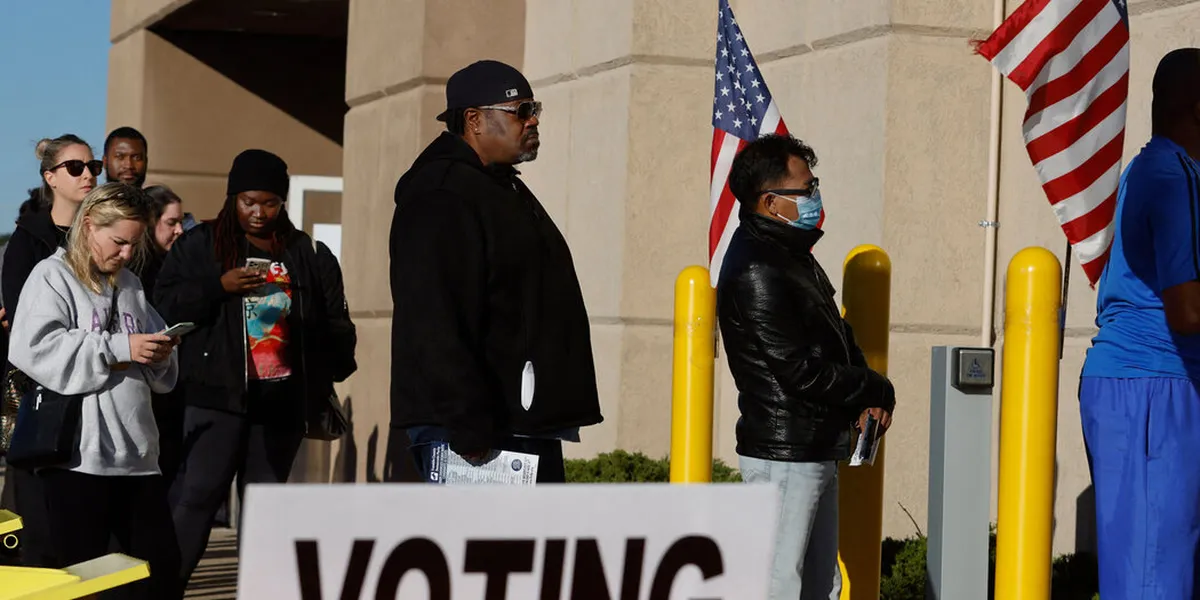 Electores haciendo fila frente a un centro de votación anticipada en Estados Unidos, junto a banderas estadounidenses y un rótulo de votación