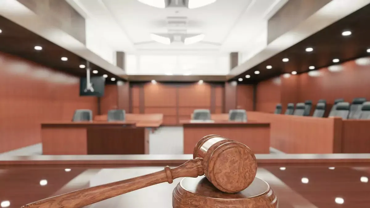 Un mazo de juez sobre su base, frente a una sala de tribunal vacía con estrados de madera al fondo