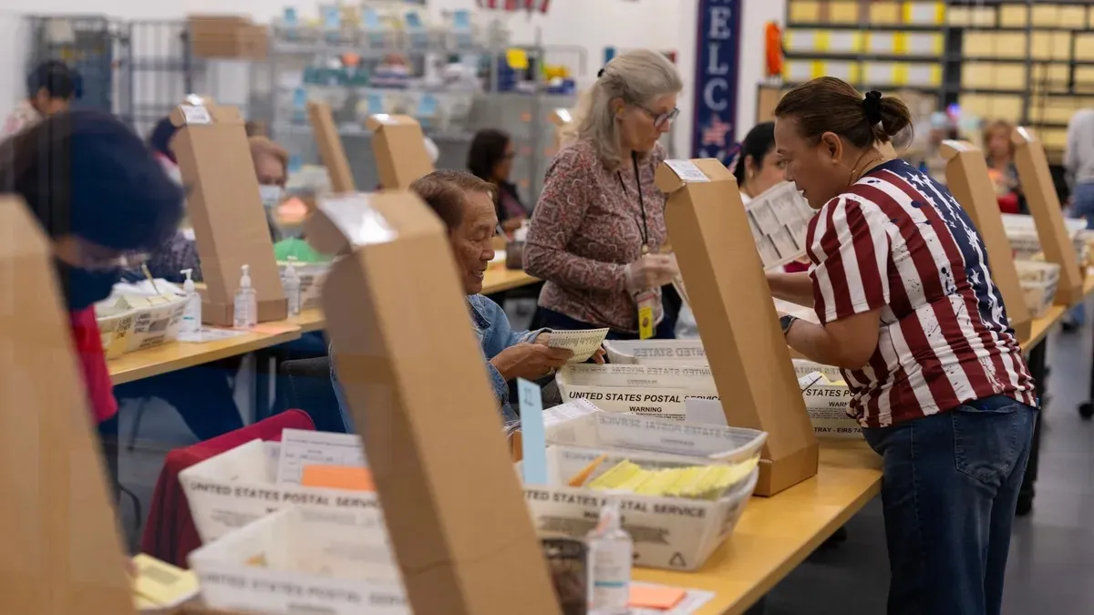 Trabajadores electorales procesando votos por correo en bandejas del servicio postal en un centro de conteo de California