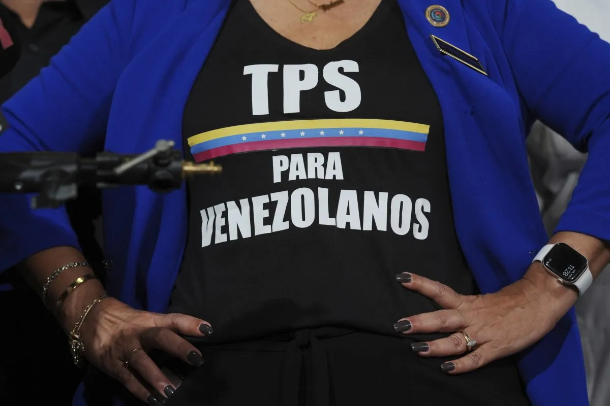 Una mujer con un blazer azul y una camiseta negra con el mensaje TPS para venezolanos y la franja tricolor de Venezuela