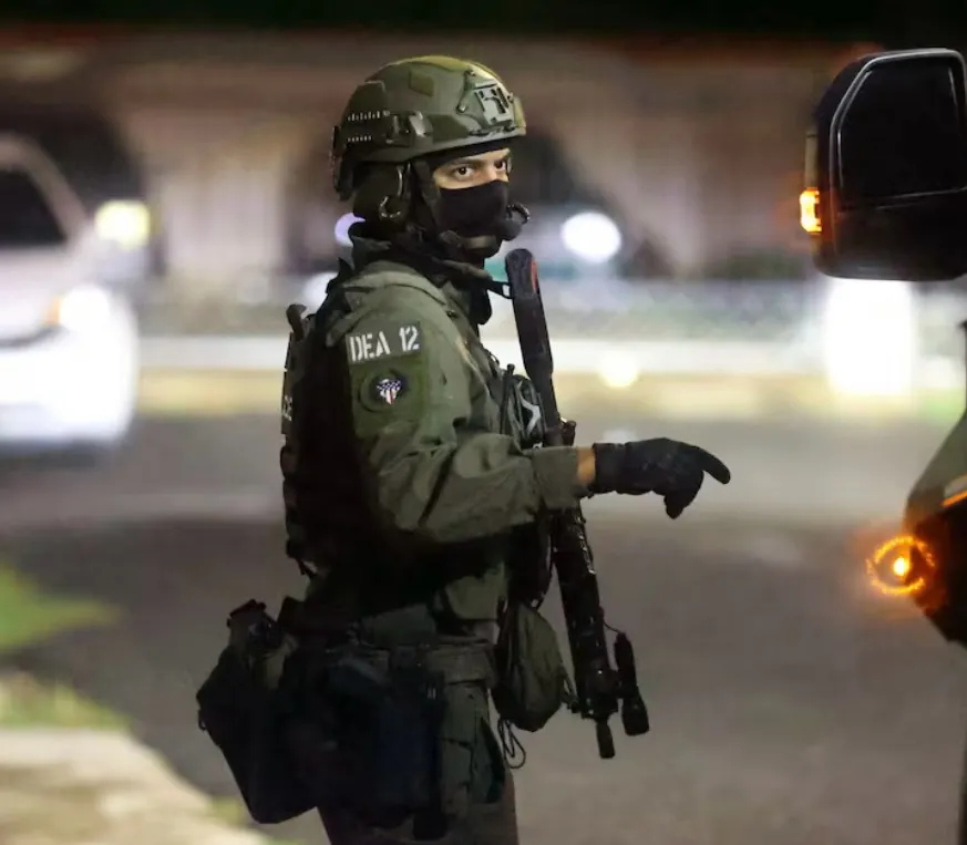 Un agente táctico identificado como «DEA 12» asegura el perímetro mientras se diligencian las órdenes.