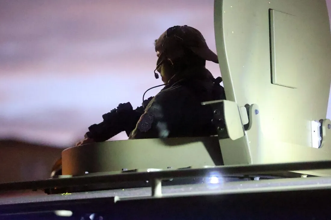 Un agente vigila desde la torreta de un vehículo blindado al caer la noche.