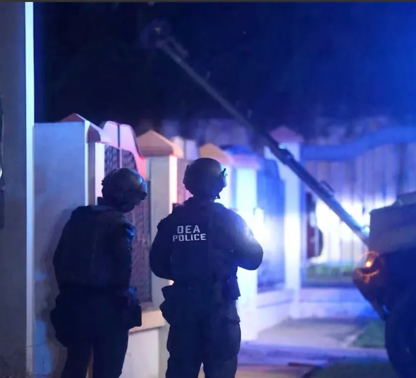 Agentes identificados como «DEA Police» frente a una residencia intervenida en la madrugada.
