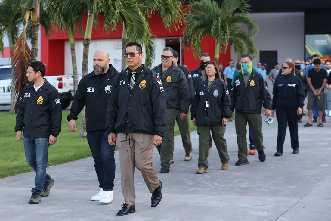 Agentes de la DEA y personal de apoyo caminan hacia el área de procesamiento de los detenidos.