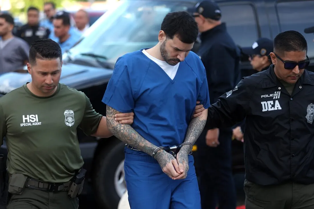 Un acusado con uniforme azul de detenido es escoltado por agentes de HSI y de la DEA.