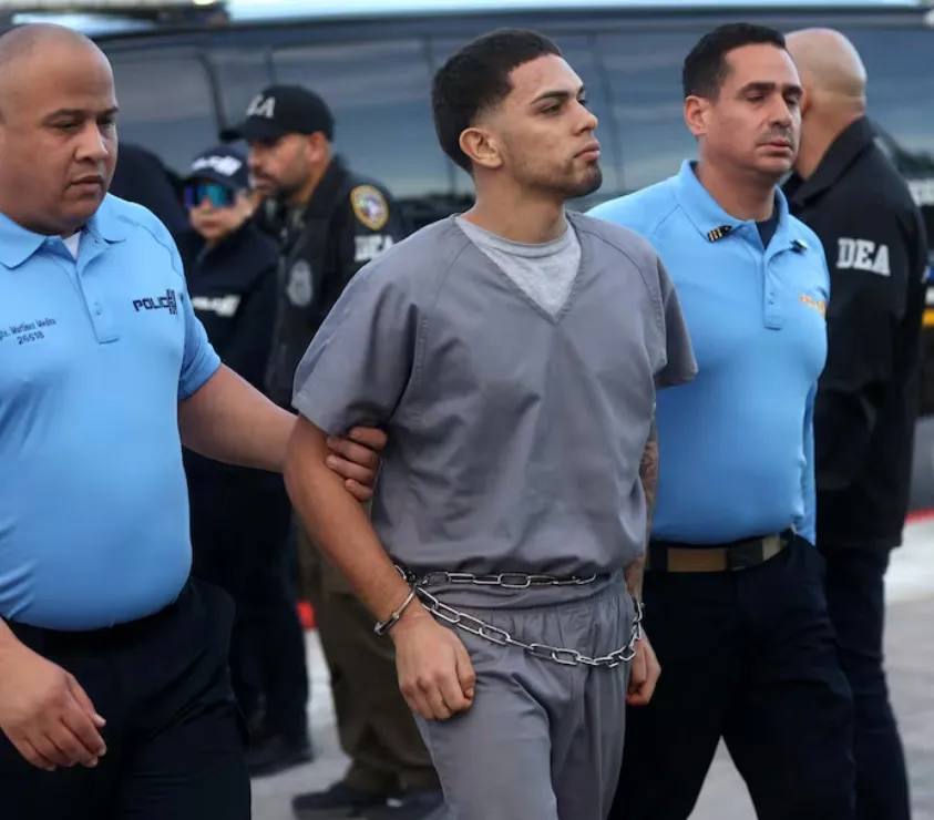 Un detenido joven, con cadenas en la cintura, es escoltado por agentes de la Policía de Puerto Rico.