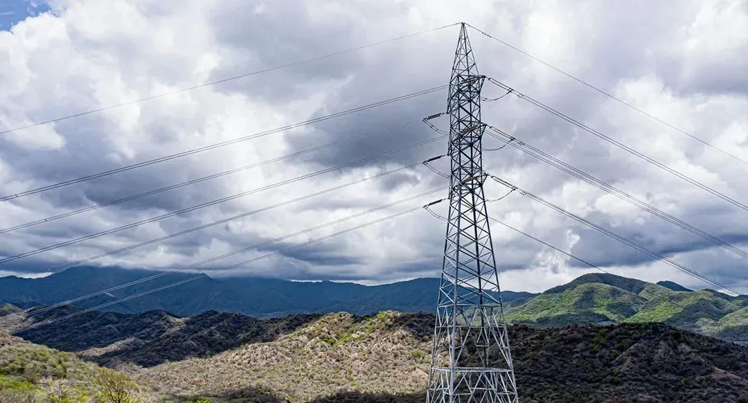 Torre de transmisión eléctrica de alta tensión con sus líneas sobre un paisaje de colinas bajo un cielo nublado