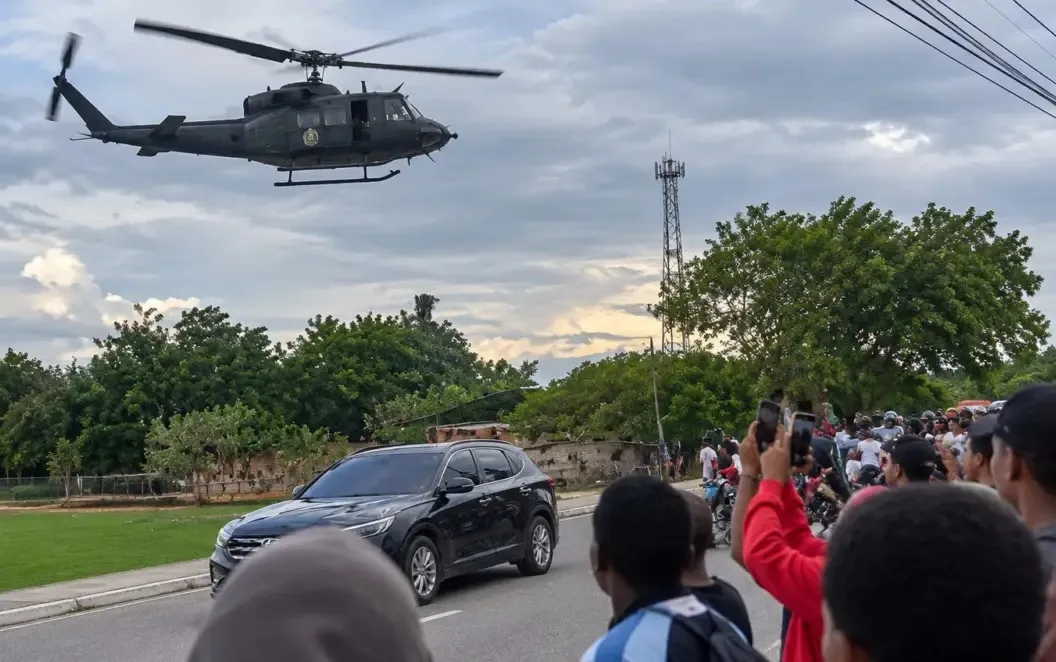 Un helicóptero militar sobrevuela a baja altura una calle de Jimaní mientras residentes lo observan desde la acera y lo graban con sus teléfonos