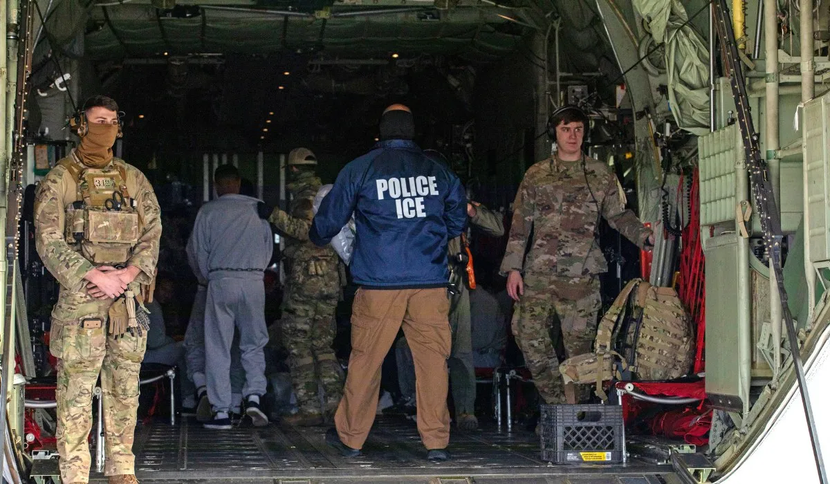Agentes de ICE y personal militar en la rampa de un avión de deportación con una persona detenida