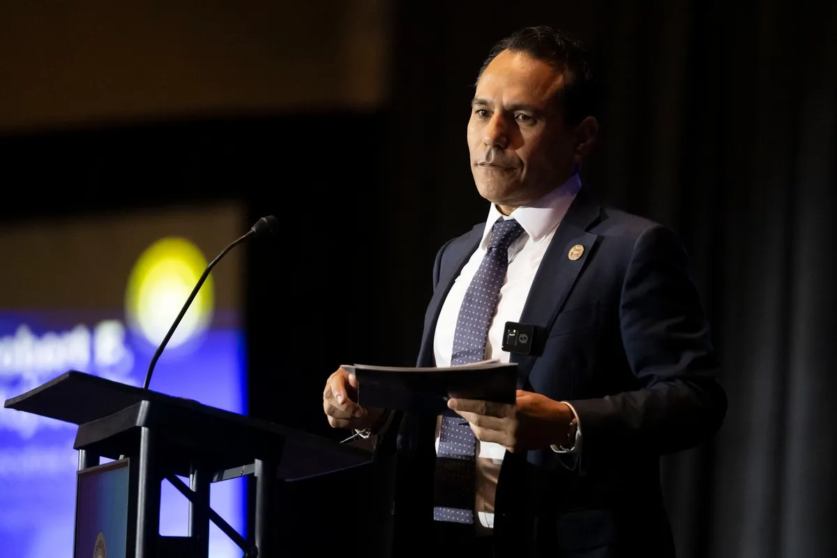 Robert Mujica, director ejecutivo de la Junta de Supervisión Fiscal, de traje oscuro y corbata, junto a un podio con micrófono durante una actividad oficial