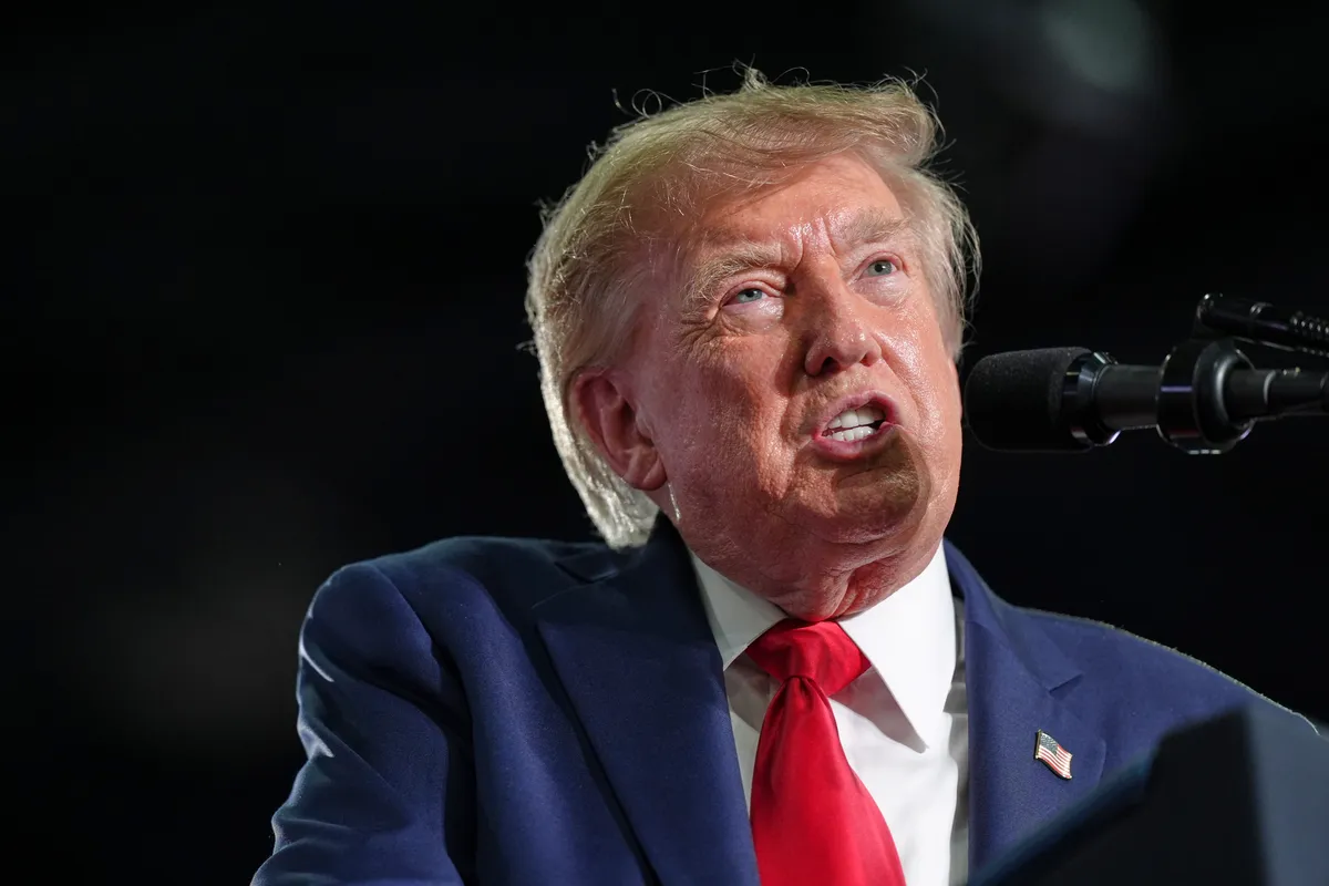 Donald Trump habla ante un micrófono durante un acto de campaña, con traje azul y corbata roja